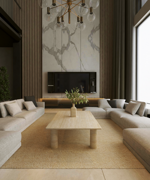 A modern living room with beige sofas around the TRAVERTABLE Rectangular Travertine Coffee Table with Solid Cylindrical Base, a tall marble accent wall, wall-mounted TV, minimal decor, and a large window filling the space with natural light.