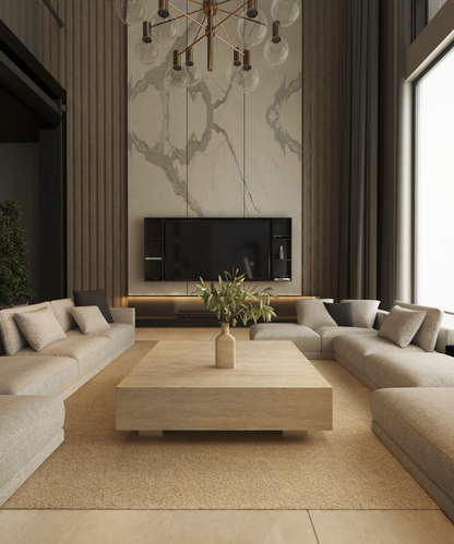 Modern living room with neutral tones, showcasing two large beige sectionals facing the TRAVERTABLE Square Travertine Coffee Table with Hidden Base. A wall-mounted TV sits above a floating console on a marble accent wall, brightened by tall windows.