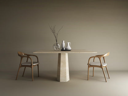 The TRAVERTABLE Square Travertine Dining Table with Rockcone Center Base features minimalist vases and branches. Two wooden chairs with white cushions sit on either side, all set against a plain beige background.