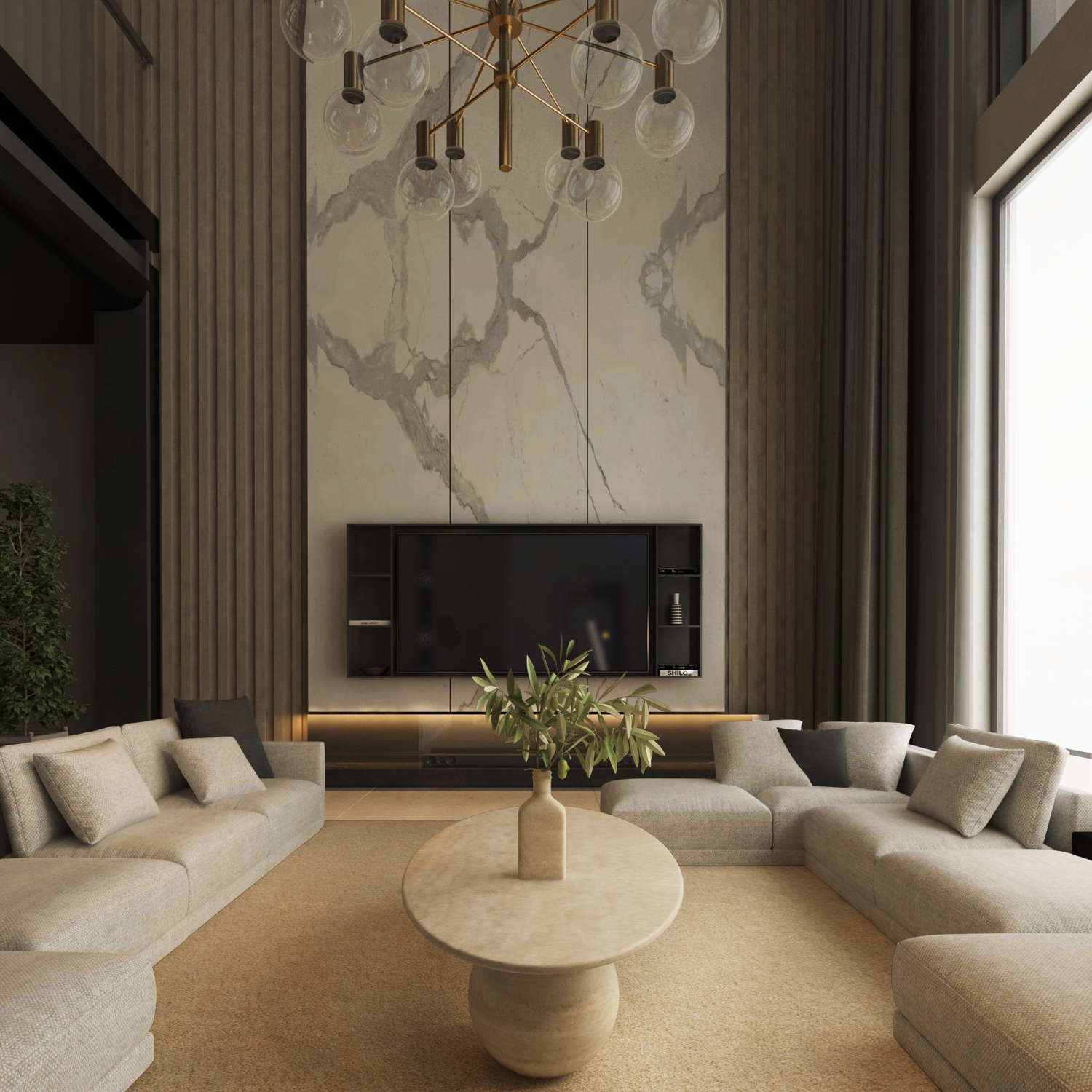 A modern living room with neutral tones features two beige sectionals around the TRAVERTABLE Ellipse Travertine Coffee Table with Stone Ball Base. A marble accent wall hosts a large TV, while tall windows and a gold chandelier brighten the space.
