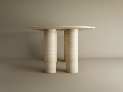 The TRAVERTABLE Oval Travertine Dining Table features a pure travertine stone tabletop and sturdy cylindrical base, offering customizable options and heirloom quality for timeless appeal against a neutral backdrop.