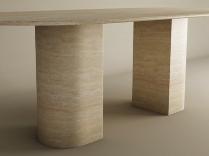 The TRAVERTABLE Oval Travertine Dining Table features a natural stone top and sloped pedestal base. Its smooth, minimalist design and customizable options make this modern heirloom piece a standout in any neutral setting.