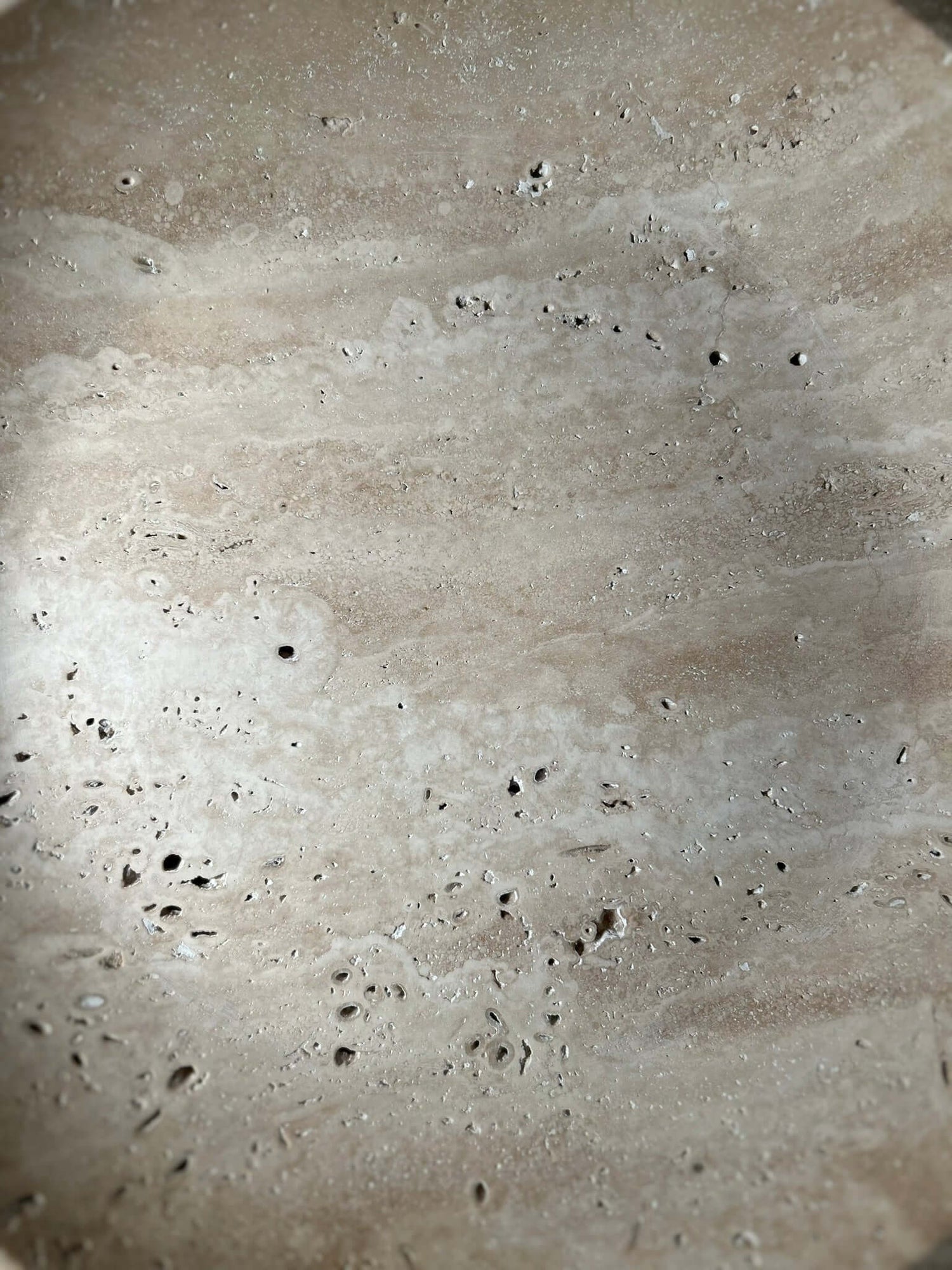 The Timeless Travertine Artisanal Bowl by Travertable features a textured beige surface with scattered small holes and speckles, reminiscent of natural travertine. Its subtle color and texture variations showcase natural artistry, offering an earthy and rustic ambiance.