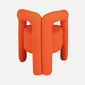 The Bold Bliss Lounge Chair by Travertable offers an artistic flair with vibrant orange fabric, a unique sculptural design, thick tubular legs, and a rounded backrest for ergonomic support and style.