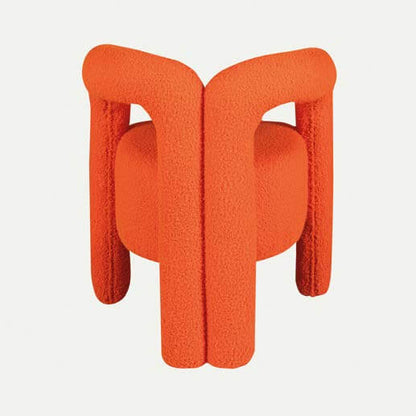 The Bold Bliss Lounge Chair by Travertable offers an artistic flair with vibrant orange fabric, a unique sculptural design, thick tubular legs, and a rounded backrest for ergonomic support and style.