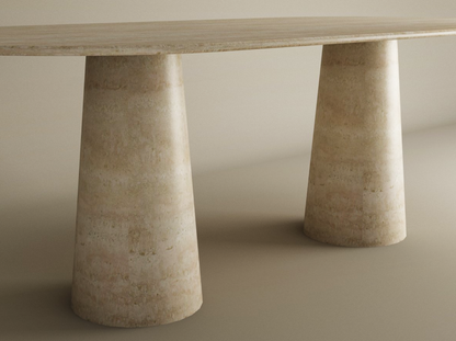 The TRAVERTABLE Oval Travertine Dining Table features a smooth, natural stone tabletop and conical pedestal bases in light beige, creating a seamless look with matching surroundings. Customizable to fit your dining space.