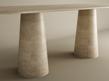 The TRAVERTABLE Rectangular Travertine Dining Table features a natural stone top and an organic travertine stone base with two wide conical pedestal legs, creating a sophisticated look on a neutral background. Customizable to your style.