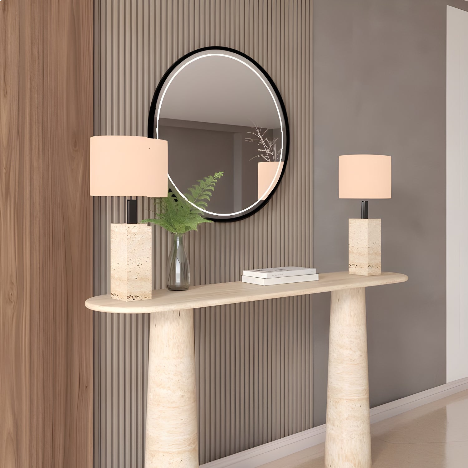 The Ovale Travertine Console Table by TRAVERTABLE, featuring an organic travertine stone base and customizable design, stands against a vertically paneled wall, topped with two lamps, a glass vase of greenery, and placed below a round black-framed mirror.