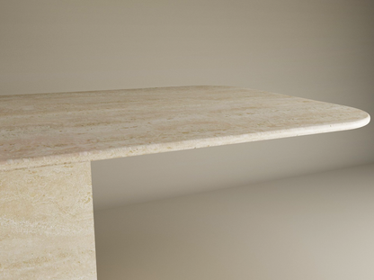 A close-up of the TRAVERTABLE Rectangular Travertine Dining Table with Block Base shows its thick natural stone top, rounded edges, and sturdy base, set against a plain background. Customizable design by TRAVERTABLE.
