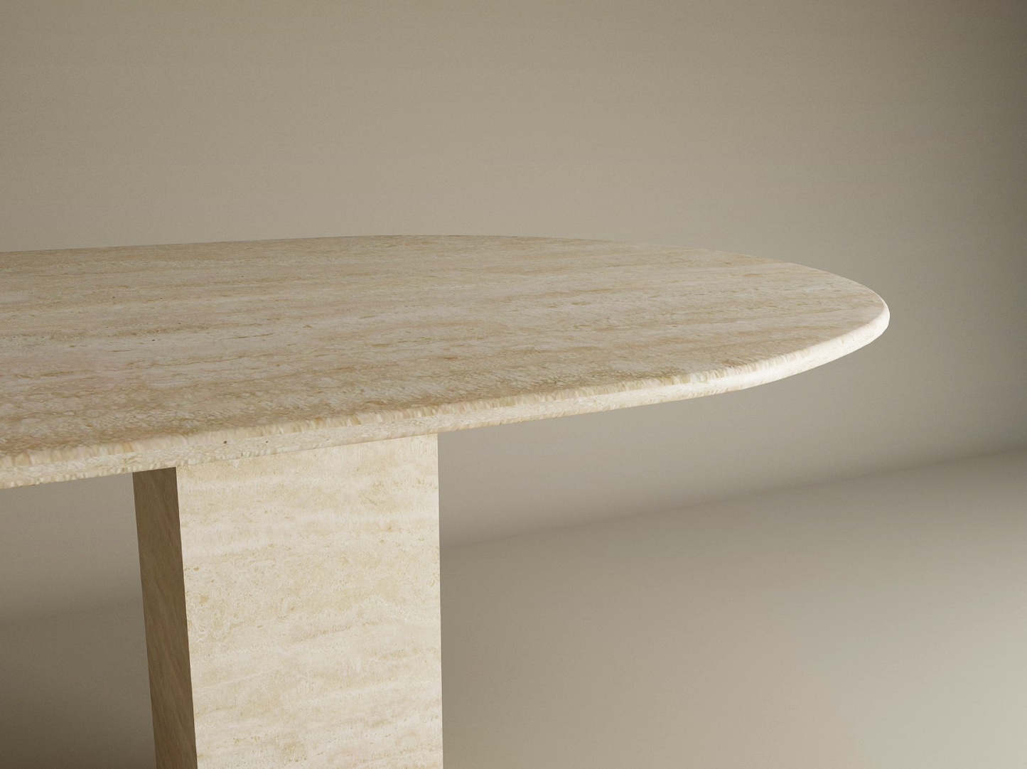 A close-up of the TRAVERTABLE Oval Travertine Dining Table, featuring a beige natural stone tabletop and a single rectangular travertine stone pedestal base, set against a plain, neutral background.