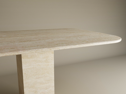 The TRAVERTABLE Rectangular Travertine Dining Table features a natural travertine stone top with rounded edges and a sturdy rectangular pedestal base, offering minimalist elegance. Customizable options are available.