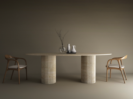 A minimalist dining setup with the TRAVERTABLE Ellips Travertine Dining Table featuring a vertical groove organic stone base, two wooden chairs with white cushions, and vases with branches as a centerpiece on a neutral-toned background.