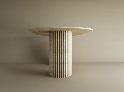 The TRAVERTABLE Oval Travertine Dining Table features a customizable organic stone top and a vertical groove base, set against a plain beige background.