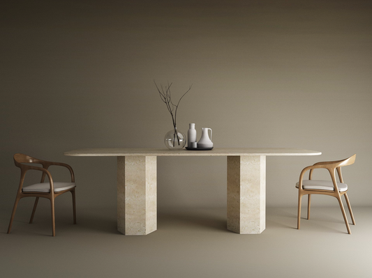 A minimalist dining setup showcases the TRAVERTABLE Rectangular Travertine Dining Table with a hexagonal organic stone base, paired with two cushioned wooden chairs and simple vase decor set against a neutral beige backdrop.