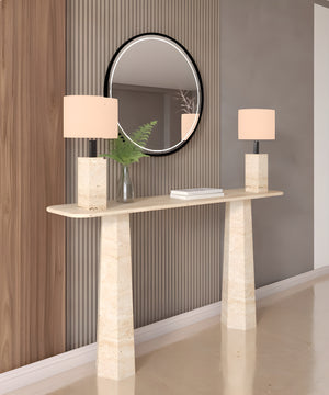 A Rectangular Travertine Console Table with Tapered Round Base by TRAVERTABLE displays two matching lamps, a vase with greenery, and a book. Placed against vertical wall paneling, it sits beneath a round mirror reflecting the room.