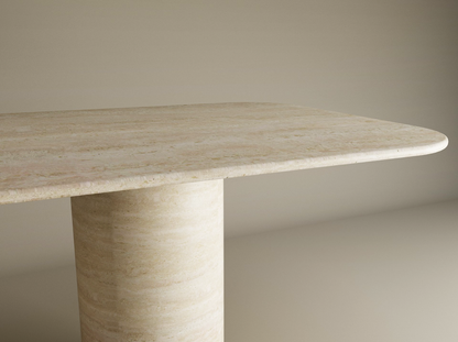 A close-up of the TRAVERTABLE Rectangular Travertine Dining Table, featuring a smooth cylindrical pure travertine stone base and rounded edges, showcases its heirloom-quality customizable tabletop against a light background.