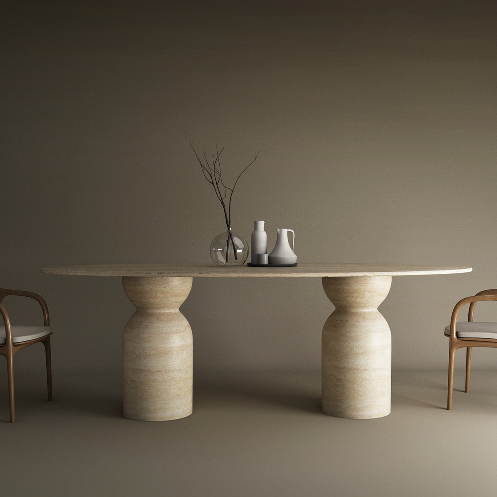 The Ellips Travertine Dining Table by TRAVERTABLE features an organic travertine stone oval top and sculptural round bases, displayed with two wooden chairs with white cushions, three vases, and a glass vessel on a plain neutral background.