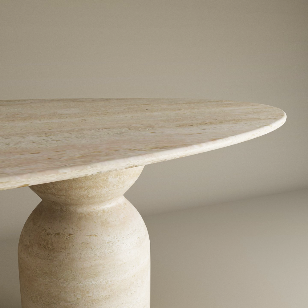 A close-up of the TRAVERTABLE Ellips Travertine Dining Table features a smooth, round natural stone top and a sculptural organic travertine base, set against a plain light background. Customization options available.