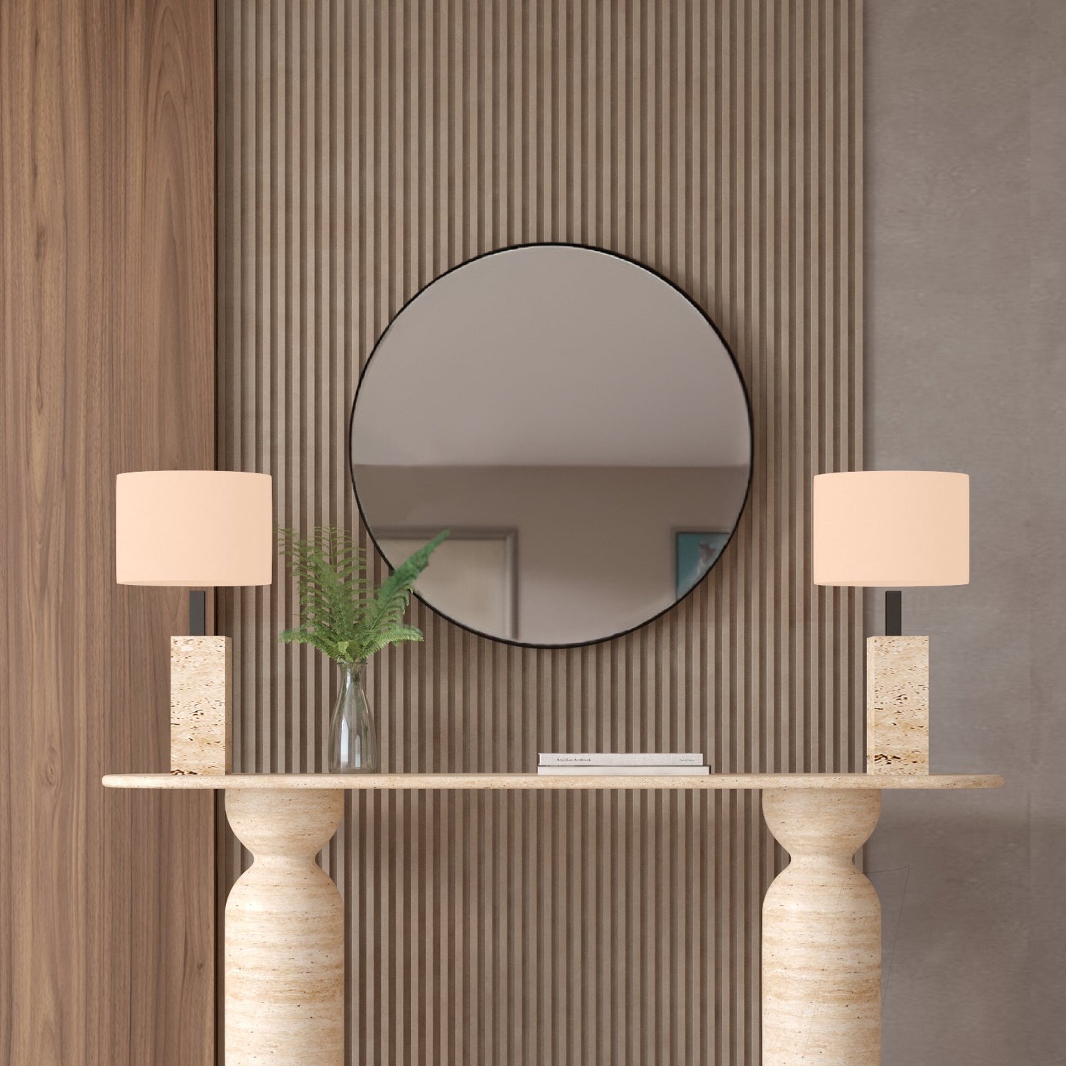 The TRAVERTABLE Ovale Travertine Console Table with a sculptural round organic stone base serves as a statement piece against a vertical wood panel wall, topped with two beige lamps, greenery in a vase, and accented by a large round mirror above.