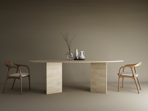 Minimalist scene with the TRAVERTABLE Ellips Travertine Dining Table (split-V Travertine stone base), two wooden chairs with white cushions, plus ceramic vases and a glass bowl with dry branches set against a beige backdrop.