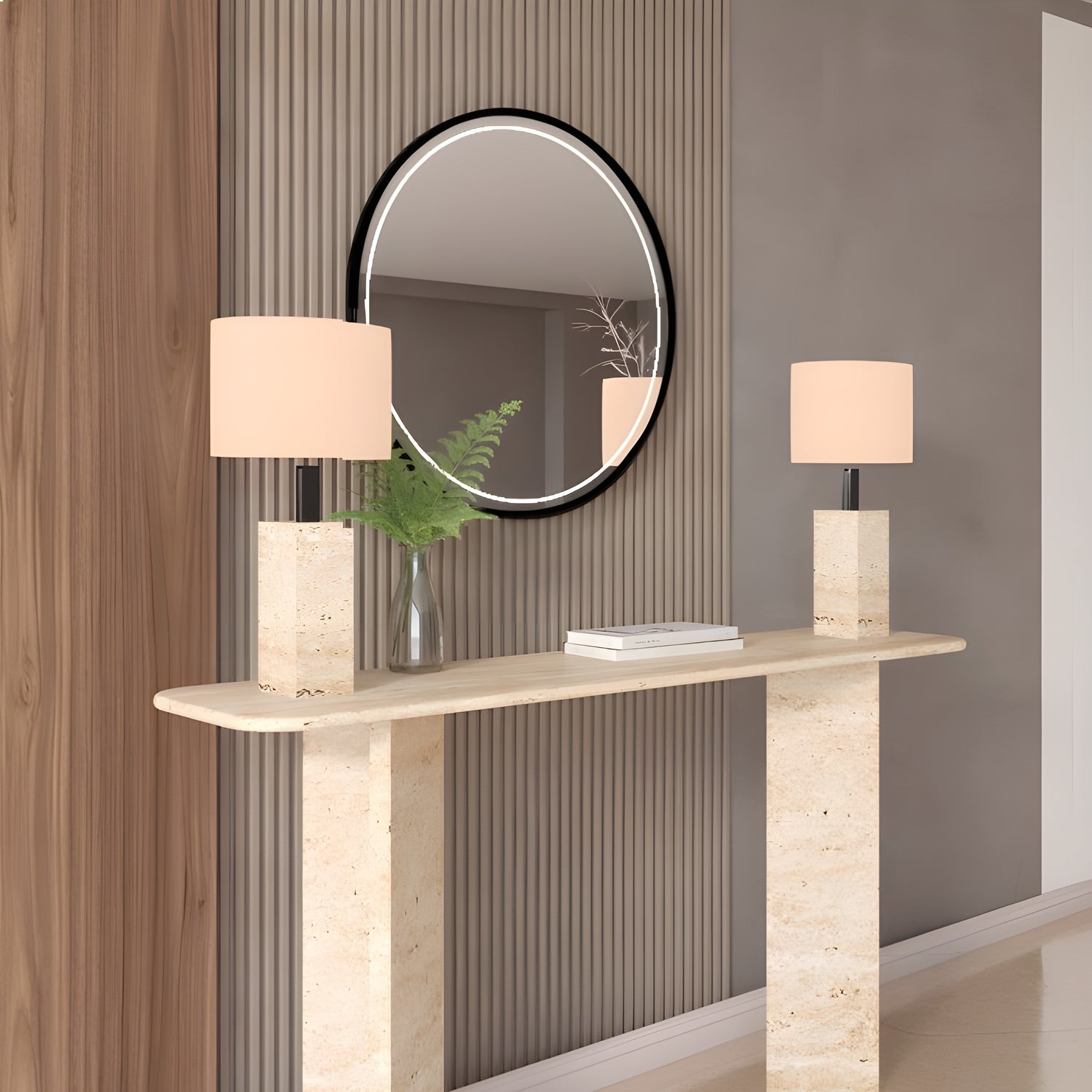The TRAVERTABLE Rectangular Travertine Console Table with Split-V Pedestal Base displays two matching lamps, a clear vase with green foliage, and a round mirror above, all set against vertically paneled walls.