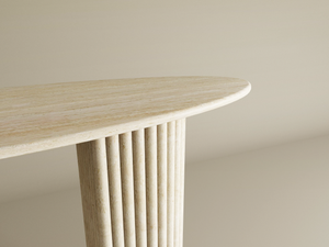 A close-up of the TRAVERTABLE Ellips Travertine Console Table with Fluted Round Base highlights its sculptural, solid stone form and refined luxury, set against a soft beige backdrop.