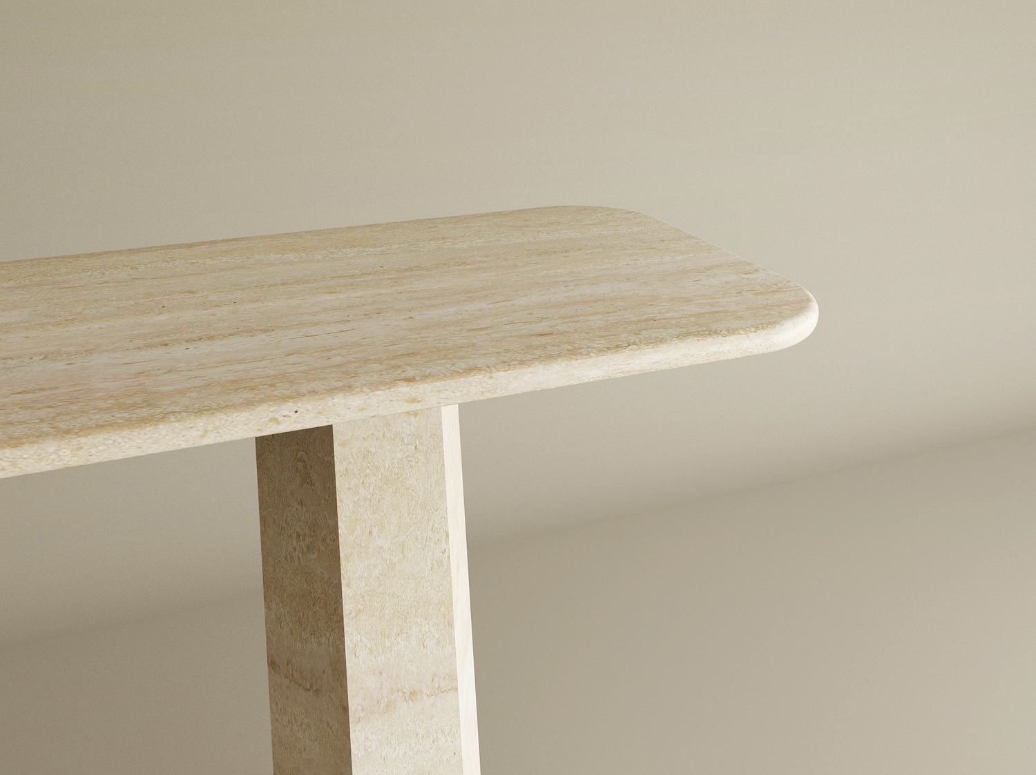 A close-up of the TRAVERTABLE Rectangular Travertine Console Table shows its light beige, stone-textured top with rounded edges and a solid travertine tapered round base, set against a plain neutral background. Customization available.