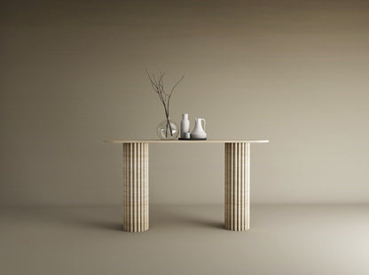 A TRAVERTABLE Ovale Travertine Console Table with Vertical Groove Base stands against a beige wall, topped with three vases—clear, white, off-white—and bare branches, creating a sculptural centerpiece in this minimal scene.
