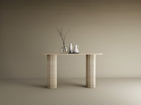 A TRAVERTABLE Ovale Travertine Console Table with Vertical Groove Base stands against a beige wall, topped with three vases—clear, white, off-white—and bare branches, creating a sculptural centerpiece in this minimal scene.