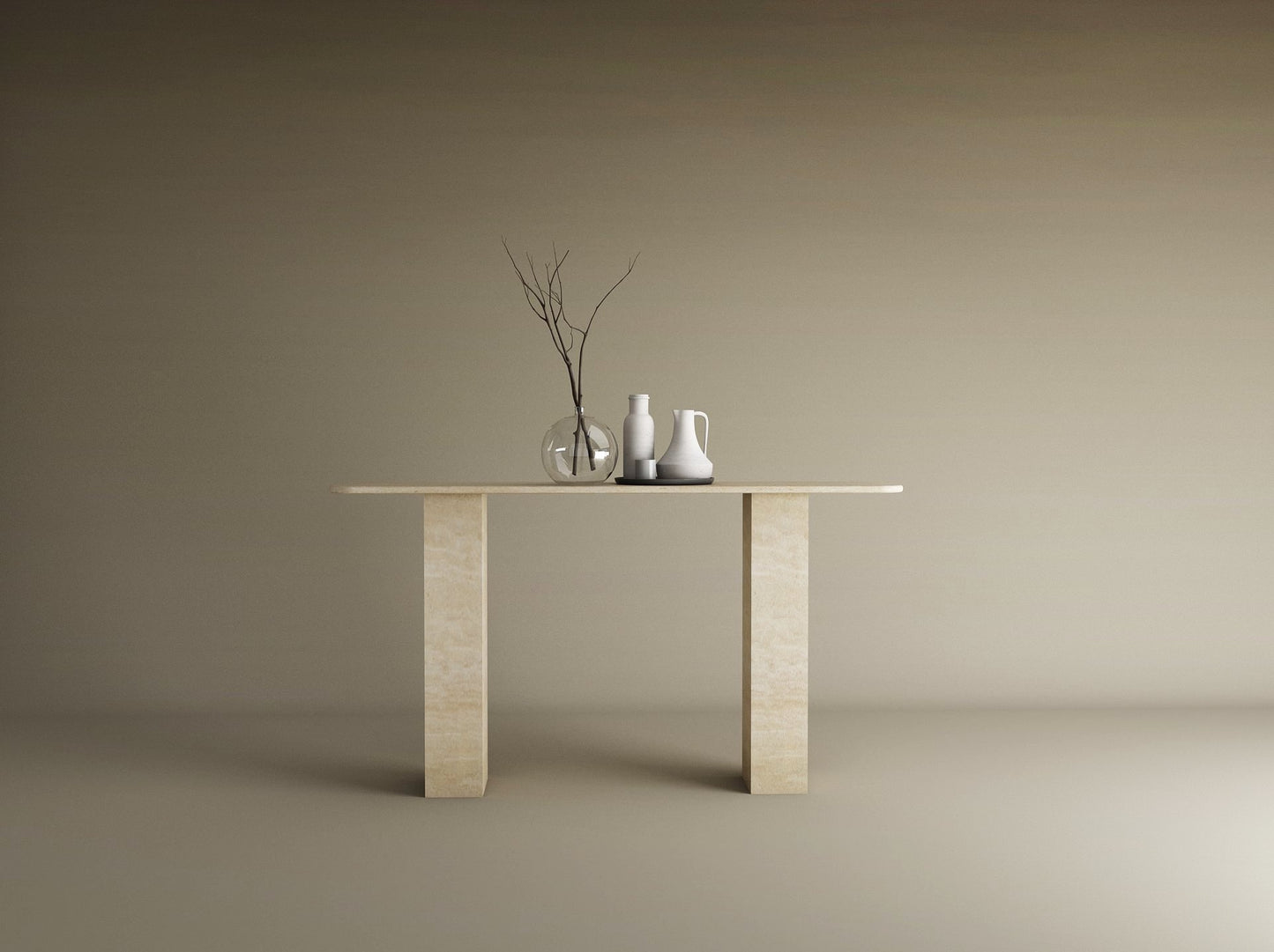 A minimalist scene with the TRAVERTABLE Rectangular Travertine Console Table, featuring a travertine stone base and top, styled with a clear vase of branches, a white pitcher, and cup against a plain beige background.