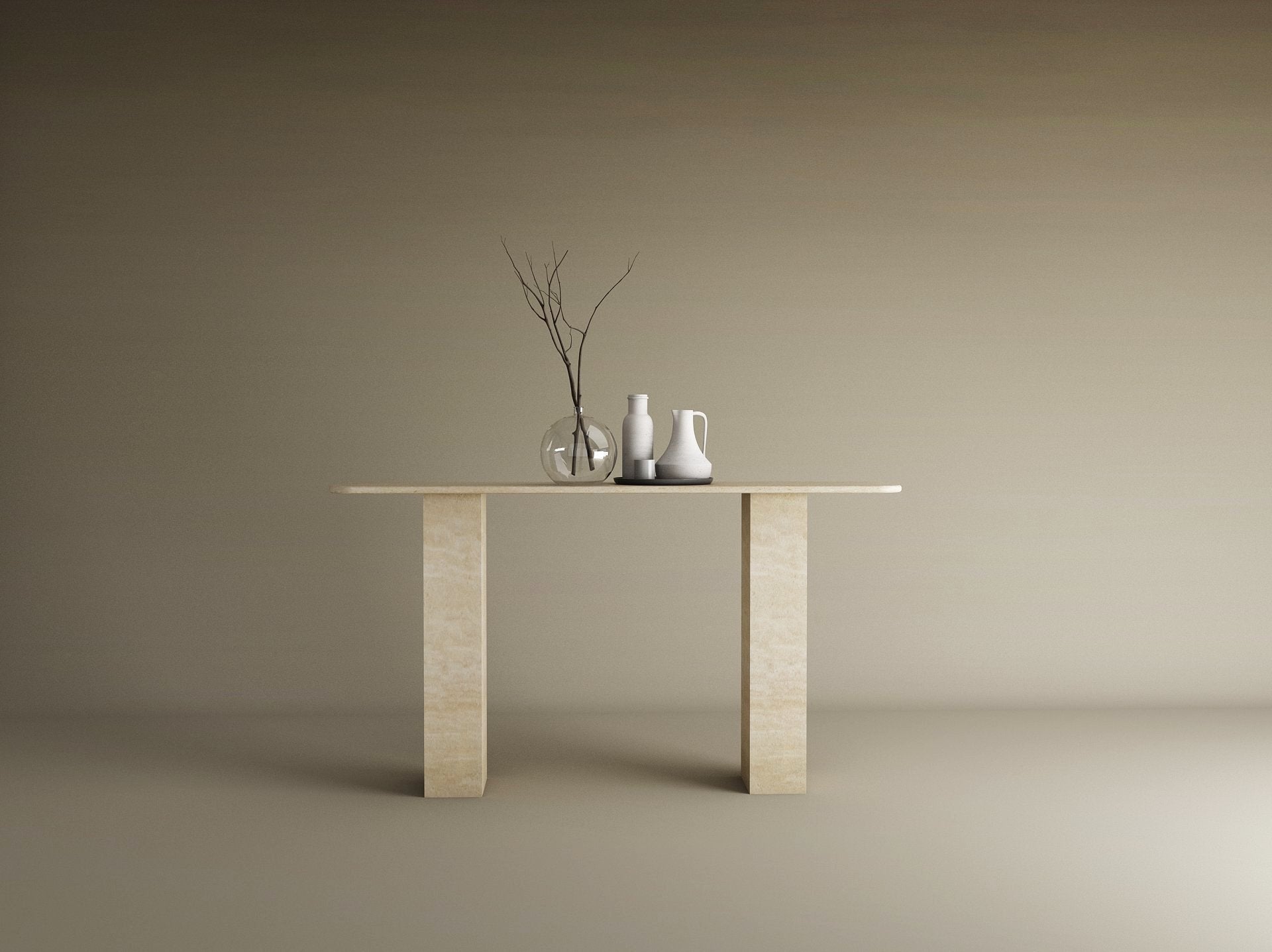 A minimalist scene with the TRAVERTABLE Rectangular Travertine Console Table, featuring a travertine stone base and top, styled with a clear vase of branches, a white pitcher, and cup against a plain beige background.