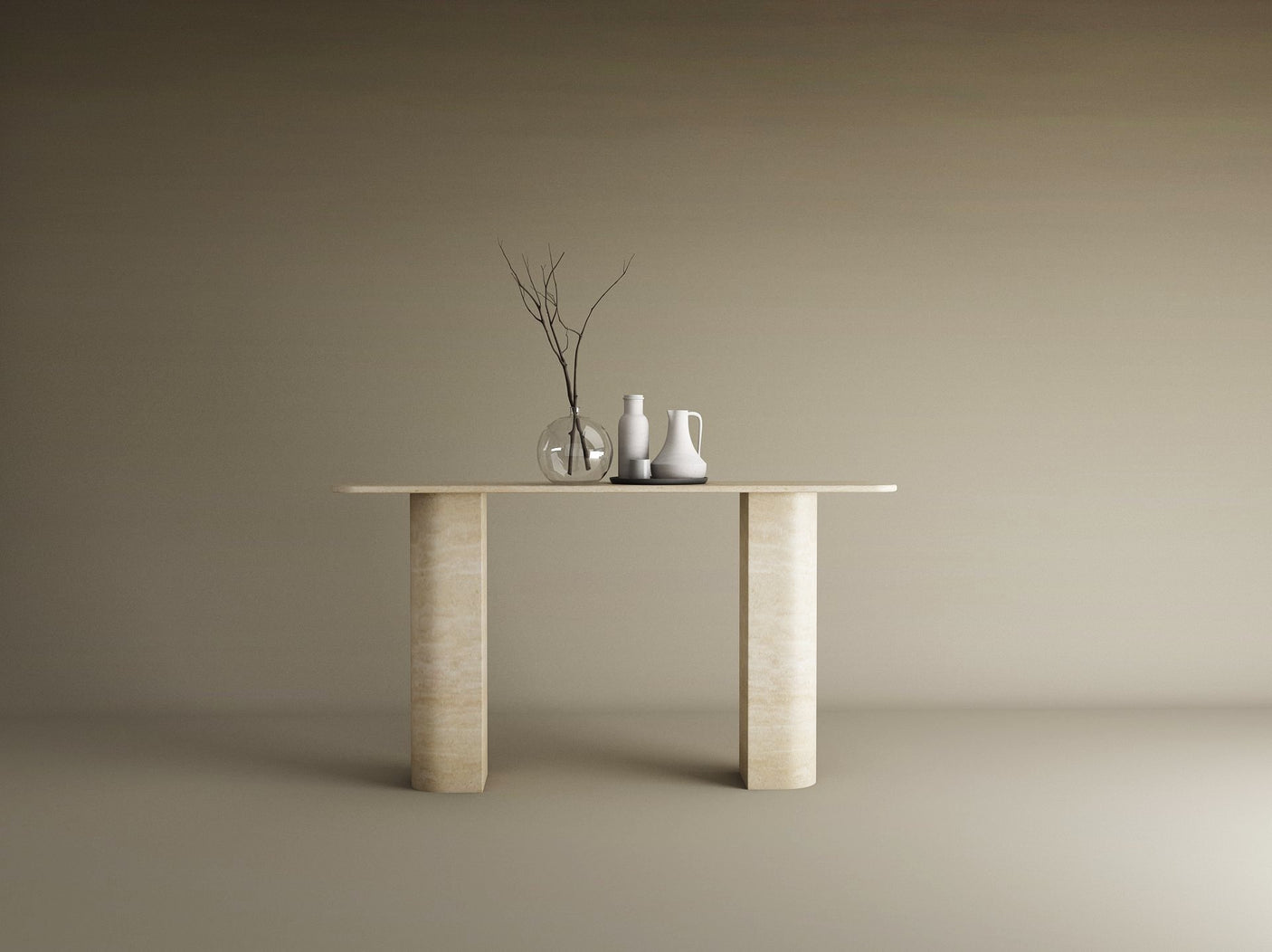 The TRAVERTABLE Rectangular Travertine Console Table with Sloped Pedestal Base in natural stone displays a glass vase with bare branches and two ceramic pitchers, set against a plain beige background.