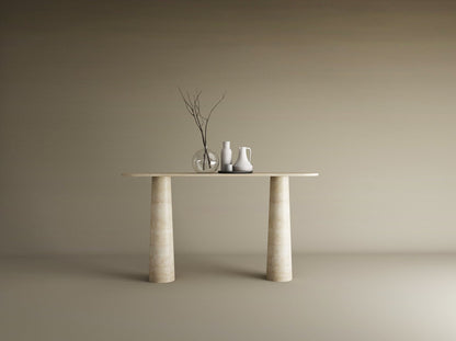 The Ovale Travertine Console Table by TRAVERTABLE features an organic travertine stone top and conical pedestal base. Three ceramic vases—one transparent, two opaque—with bare branches sit against a plain beige background.