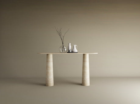 The Ovale Travertine Console Table by TRAVERTABLE features an organic travertine stone top and conical pedestal base. Three ceramic vases—one transparent, two opaque—with bare branches sit against a plain beige background.