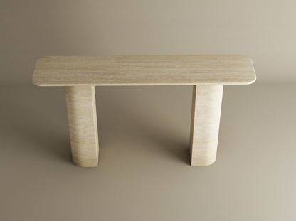 The TRAVERTABLE Rectangular Travertine Console Table features a customizable natural stone top and a sloped pedestal base, offering a minimalist sculptural design perfect against a plain beige background.