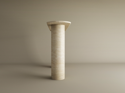 The TRAVERTABLE Ovale Travertine Console Table features a smooth, cylindrical pure travertine stone base and flat round top, standing elegantly on a beige floor against a matching background. The surface is slightly textured and customizable.