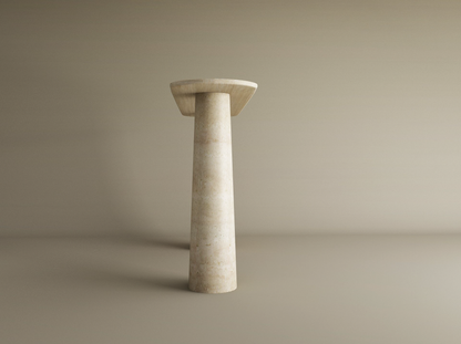 The TRAVERTABLE Ovale Travertine Console Table features a tall, conical travertine stone base and circular top, showcasing sculptural elegance in a minimalist setting. Customizable for your space.