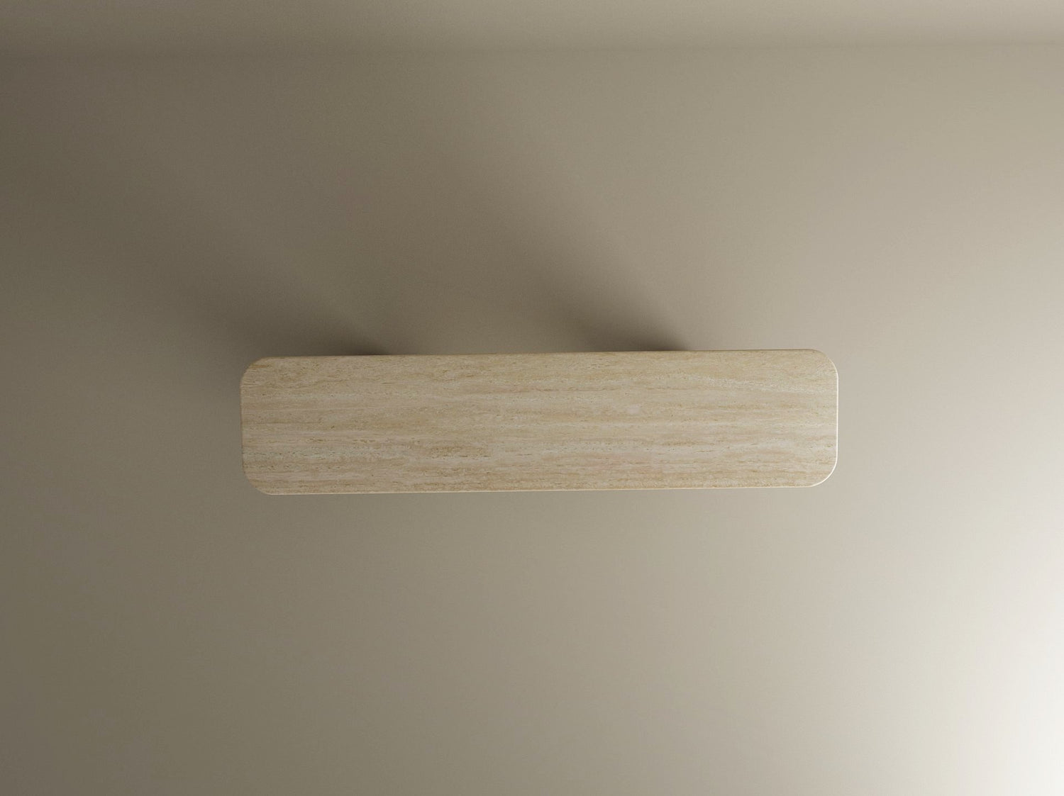 A Rectangular Travertine Console Table with a split-V stone base by TRAVERTABLE is set against a light beige wall, casting soft shadows on both sides. The image is captured from a top-down angle.