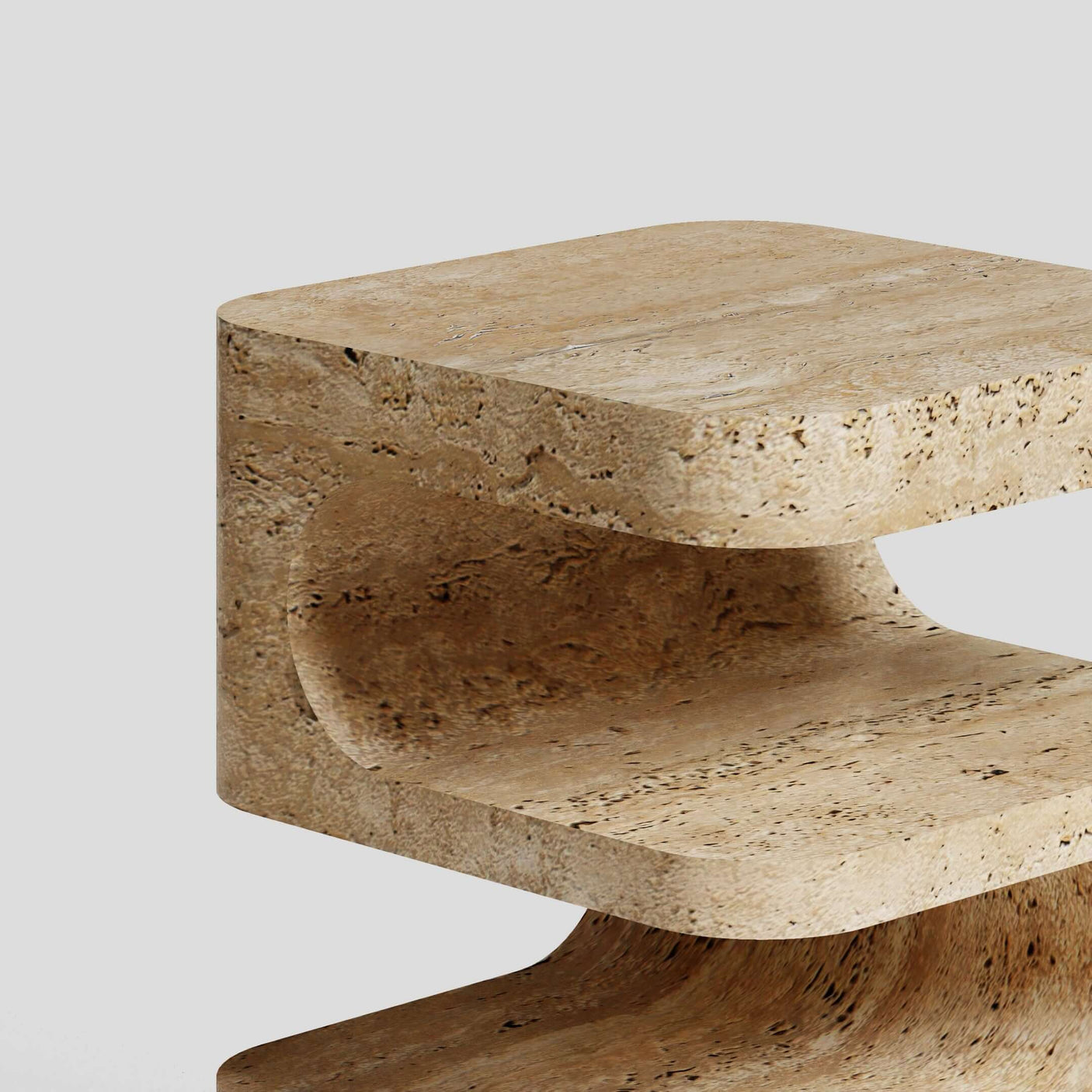 A close-up of the Serenity Block Travertine Table by Travertable reveals its C-shaped design with smooth, rounded edges and a natural stone texture against a plain light gray background. This elegant table melds functionality with timeless style.