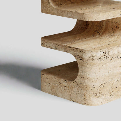 Close-up of Travertables Serenity Block Travertine Table, showcasing smooth curves and a natural texture against a gray background. The light casts a subtle shadow, highlighting its unique patterns and earthy tones.