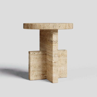 The Travertable Travertine Scepter Side Table features a unique architectural design in honed travertine with a round top and cross-shaped base. Its natural stone texture makes it an ideal centerpiece for modern coffee tables, set against a plain light gray background.