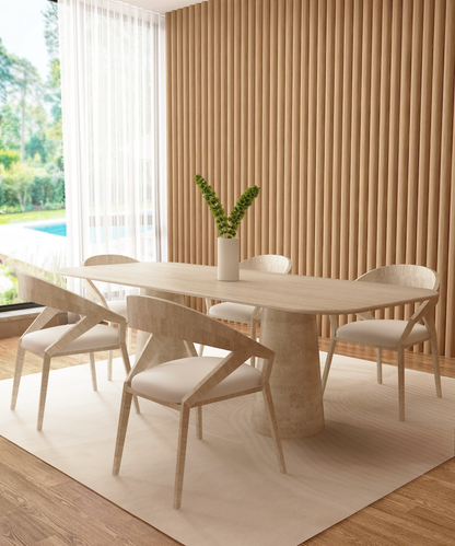 A modern dining room with a TRAVERTABLE Rectangular Travertine Dining Table featuring an organic stone conical pedestal base, six matching white-cushioned chairs, a white vase centerpiece, wood paneling, and large windows with views of lush greenery.