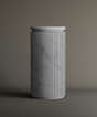 The TRAVERTABLE Carrara Round Marble Pedestal Vanity Sink features a tall, cylindrical form with vertical grooves and smooth Carrara marble surface, highlighted by subtle gray veining against a neutral background.