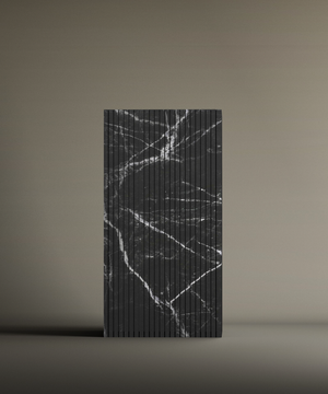The TRAVERTABLE Nero Marquina Square Fluted Marble Pedestal Vanity Sink is a rectangular, upright sink with vertical grooves and a black surface featuring irregular white marble-like veins, set against a plain beige background.