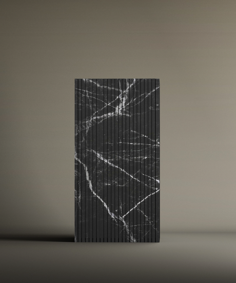 The TRAVERTABLE Nero Marquina Square Fluted Marble Pedestal Vanity Sink is a rectangular, upright sink with vertical grooves and a black surface featuring irregular white marble-like veins, set against a plain beige background.