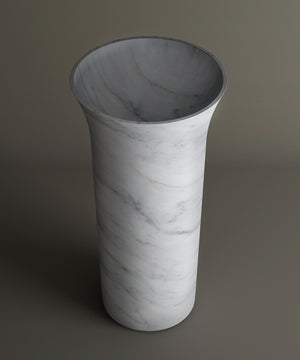 The TRAVERTABLE Carrara Marble Cylinder Pedestal Vanity Sink features a tall, cylindrical shape with a flared opening and subtle gray veining, evoking the timeless beauty of high-end marble bathroom sinks.