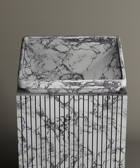 The TRAVERTABLE Calacatta Square Marble Pedestal Vanity Sink, with gray and black veining and vertical grooves, creates a bold marble centerpiece against a plain gray background.