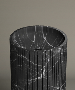 The TRAVERTABLE Nero Marquina Round Fluted Marble Pedestal Vanity Sink features black marble with white veining, fluted grooves, and a polished rounded basin—an elegant contemporary piece set against a beige background.