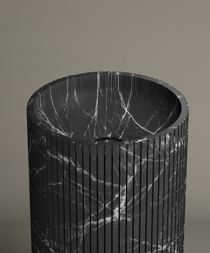 The TRAVERTABLE Nero Marquina Round Fluted Marble Pedestal Vanity Sink features black marble with white veining, fluted grooves, and a polished rounded basin—an elegant contemporary piece set against a beige background.