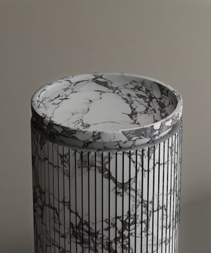 The TRAVERTABLE Calacatta Round Marble Pedestal Vanity Sink, featuring dark gray veining and fine vertical grooves, stands against a beige background. Its flat top highlights Italian craftsmanship and striking marble patterns.